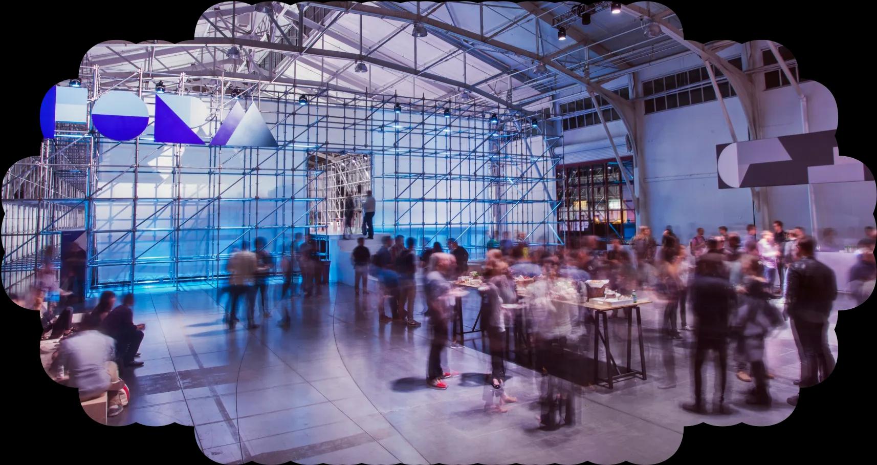 Dozens of event attendees walking through a large hangar-like space.